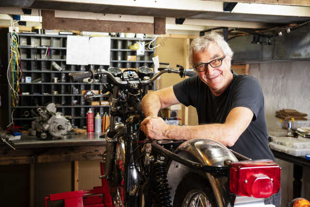 Älterer Mann in einer Werkstatt mit einem alten Motorrad