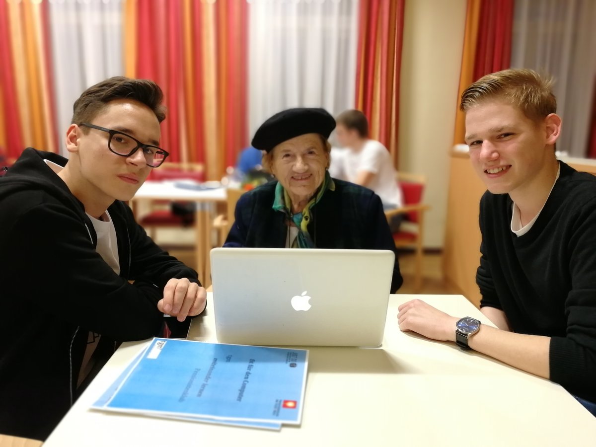 Eine ältere Dame mit zwei jungen Schülern vor einem Laptop