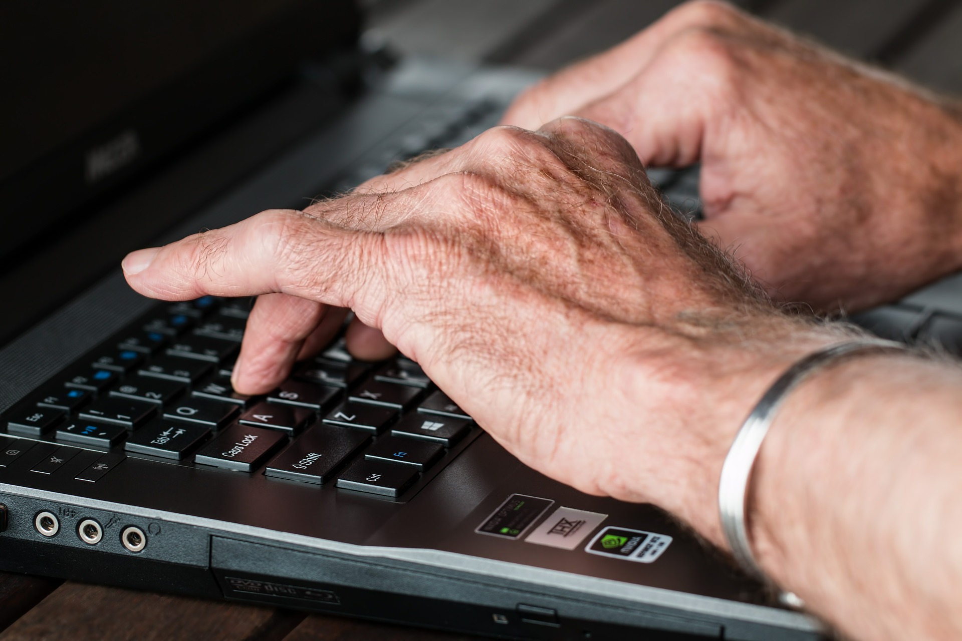Hände eines älteren Menschen auf einer Computertastatur
